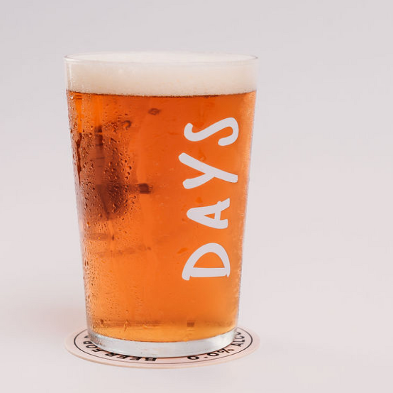 A pint glass filled with amber beer, labeled 'DAYS,' on a coaster.